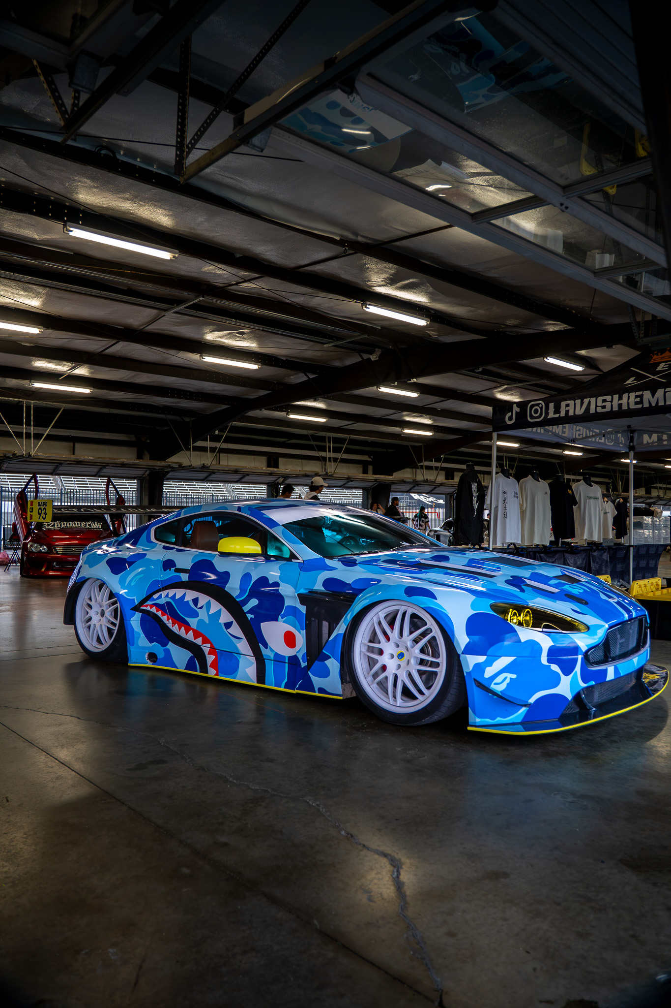 Blue camo-wrapped Aston Martin Vantage with shark graphic at a car show