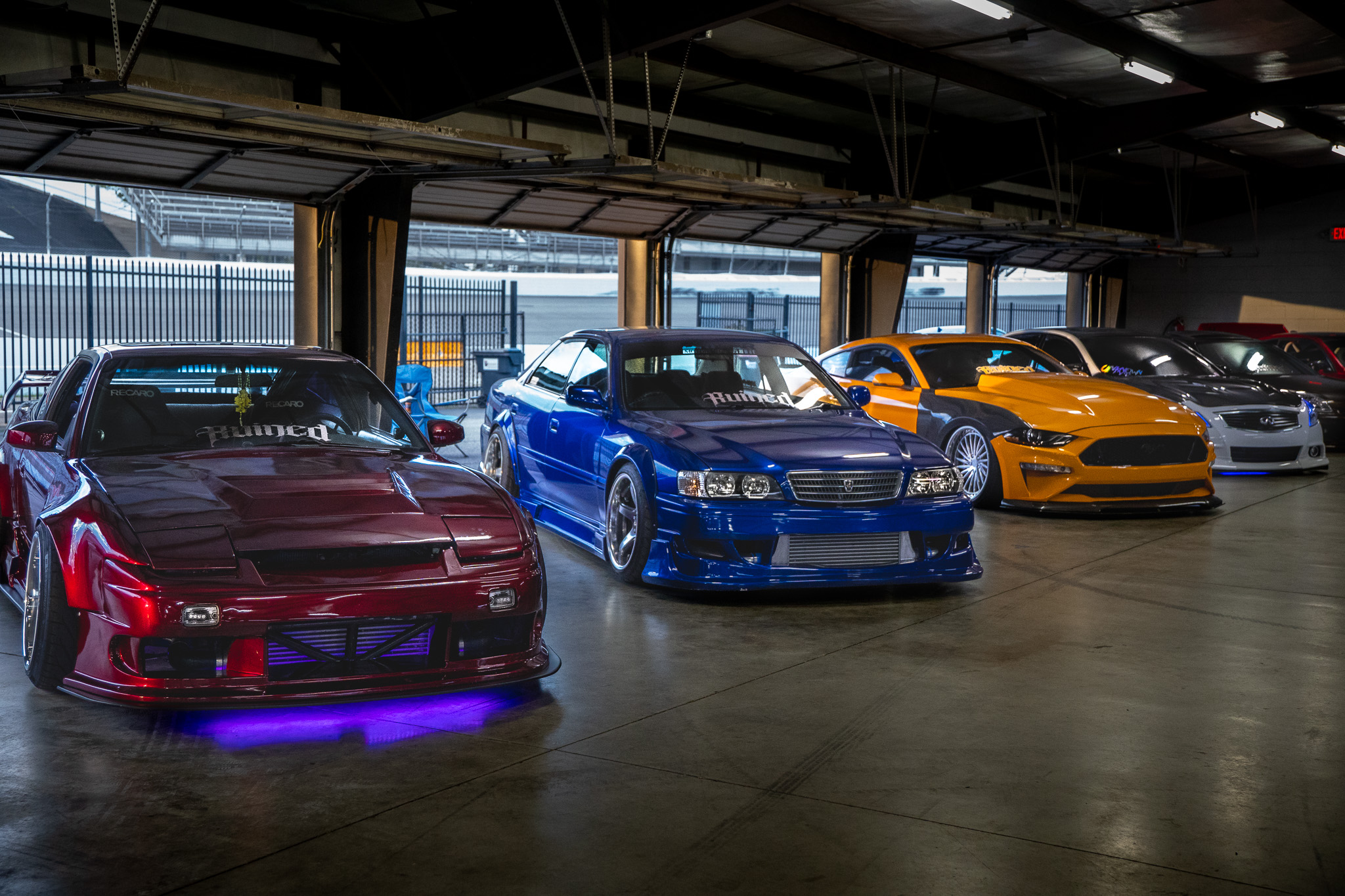 Lineup of modified cars inside a garage bay at a car meet