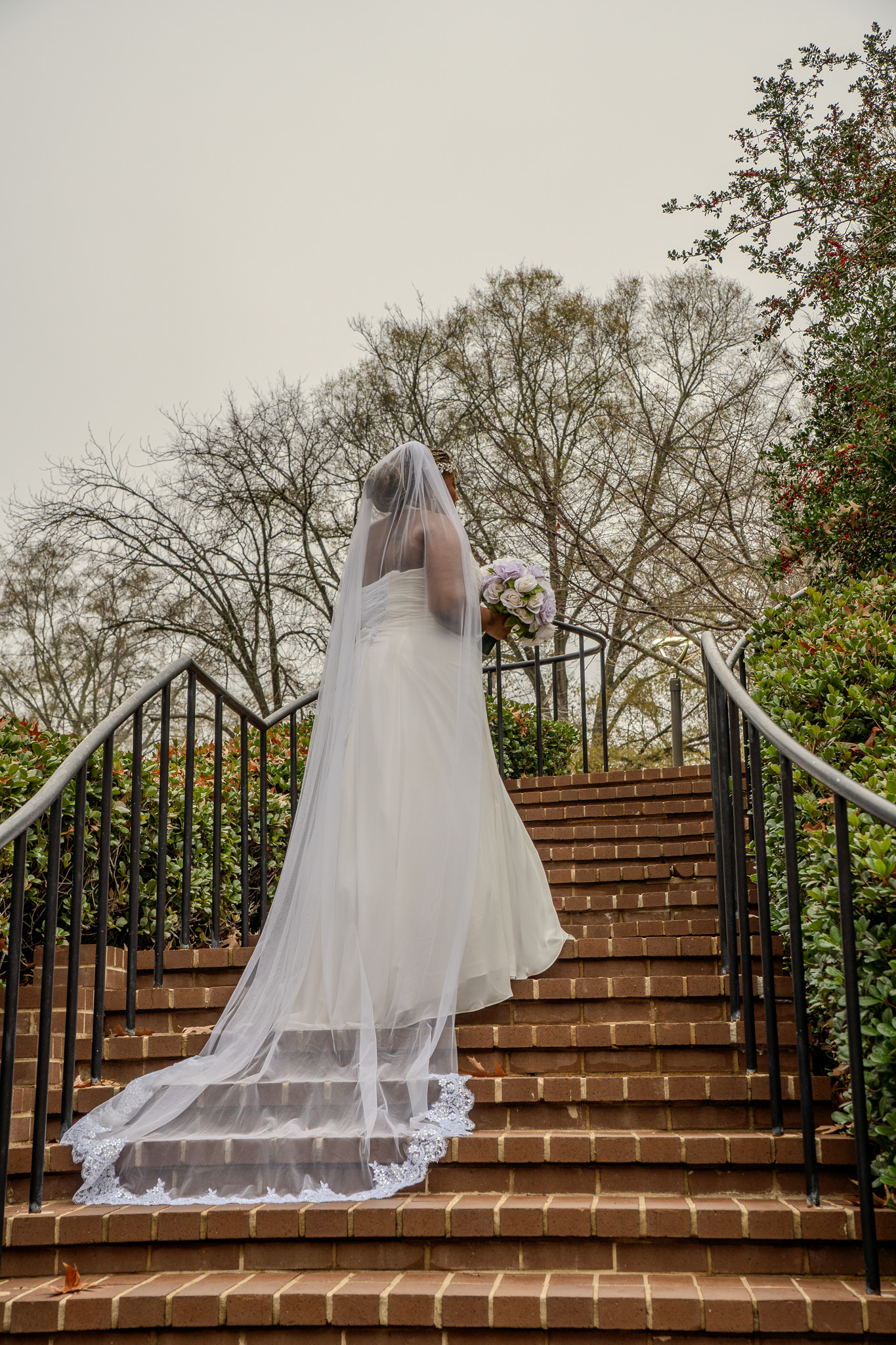 Bride ascending brick stairs, veil flowing, overcast sky