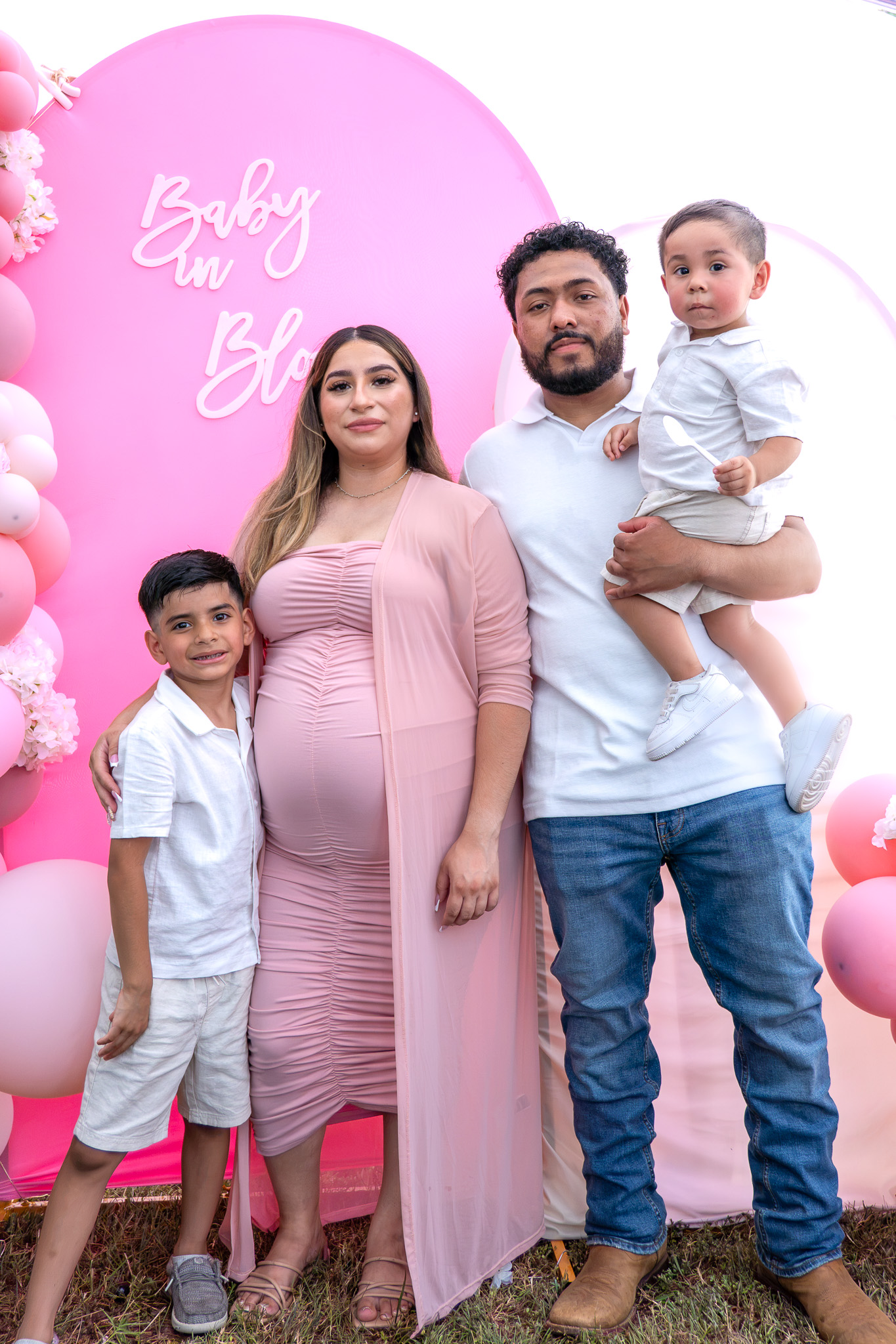 Full family portrait at a baby shower with pink balloon backdrop
