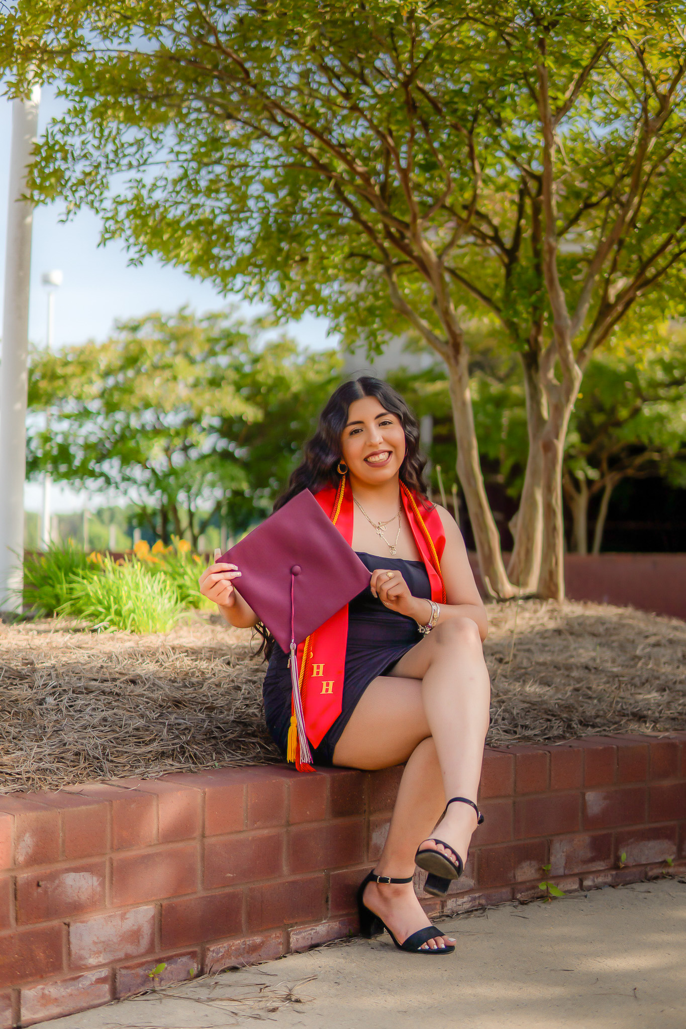 Graduate in cap and gown seated on a brick wall
